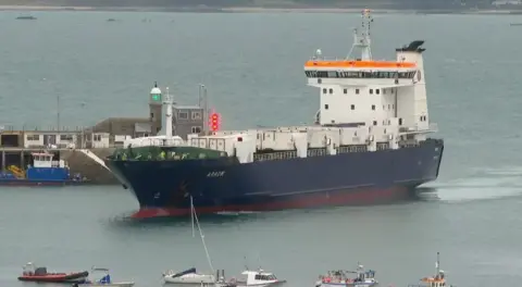 A ship with a blue hull and a white cabin entering St Peter Port Harbour, it has the word Arrow in the front of the ship. 